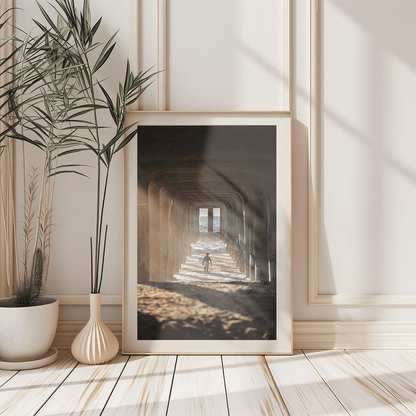 a fine art photo of a surfer under a pier with sunlight casting shadows in a wood frame leaning up against a white wall with plants along side